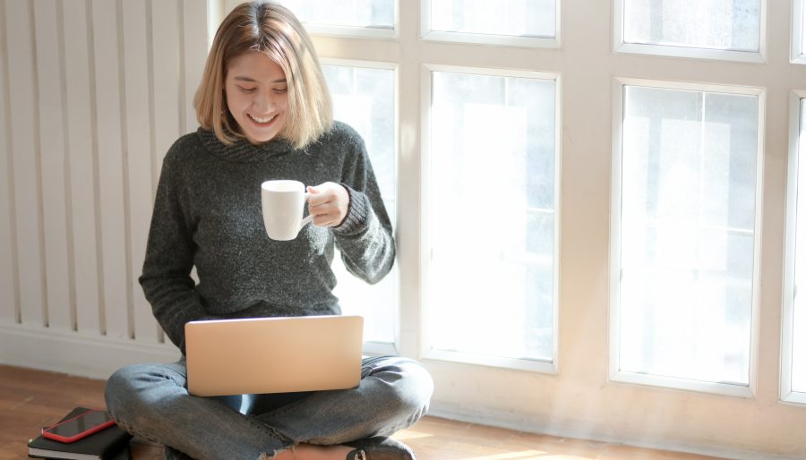 Image of a woman sat cross legged looking at her computer with a cup.