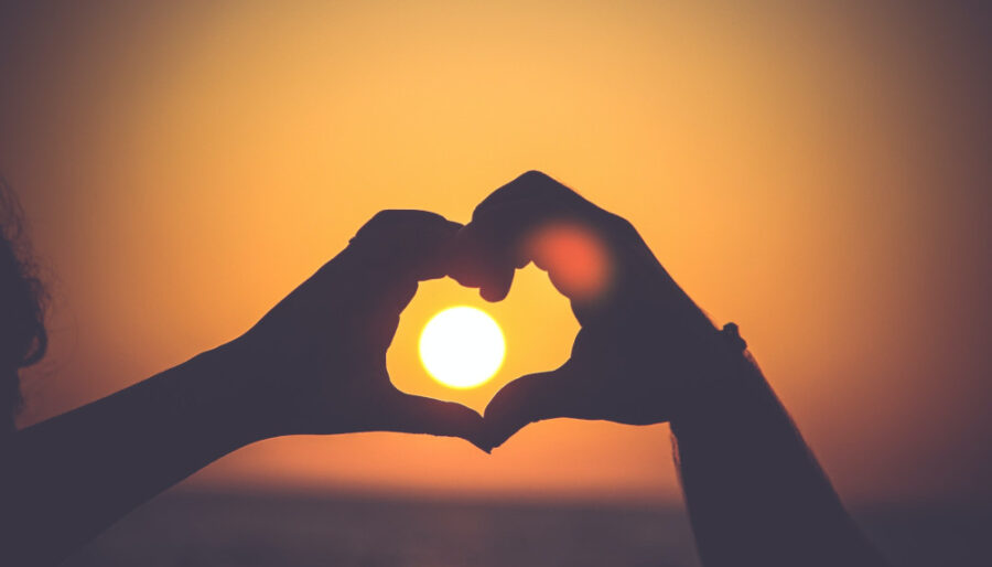 Image of two hands making a heart with a sunset in the background