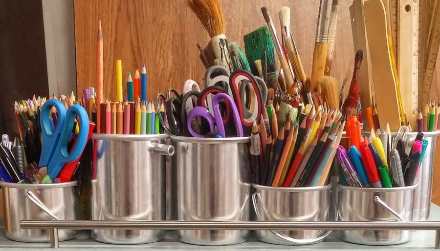 Image of various arts and crafts utensils in pots. There are scissors, paint brushes, pens, rulers and colouring pencils.